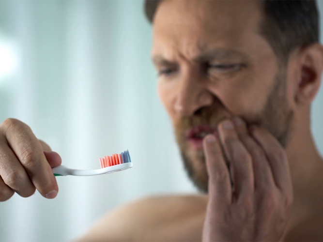 man with bleeding gums holding his cheek in pain and holding his toothbrush in his other hand